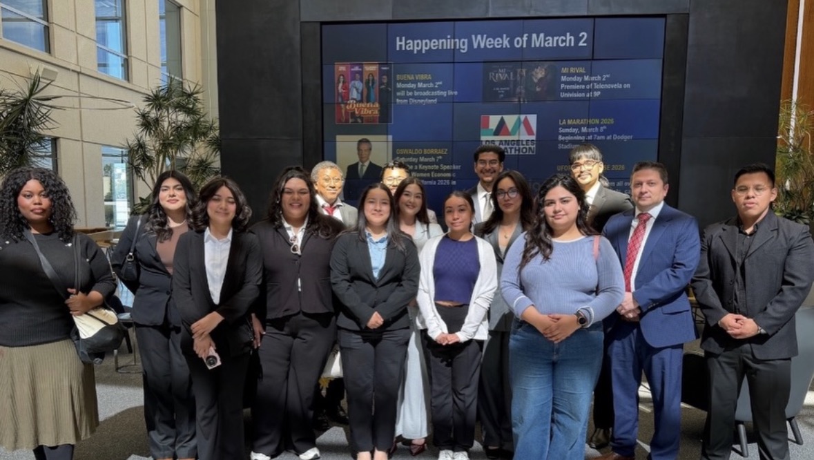 LSBA members in professional attire posing together in a university lobby in front of a large campus events display screen.